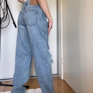H&M ljusblå ripped jeans - Säljer ett par H&M jeans i ljusblå denim med raka ben och snygga slitningar på båda knäna. Jeansen har hög midja, fem fickor och en avslappnad, loose passform. Perfekta för en chill och trendig look.