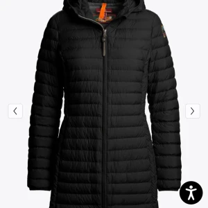 Svart lång dunjacka Parajumpers - Svart lång dunjacka från Parajumpers med huva och quiltad design. Jackan har dragkedja framtill, diskret logga på ärmen och en figurnära passform. Perfekt för kalla dagar när du vill hålla stilen och värmen.