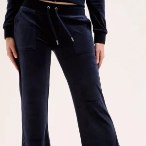 Juicy cotoure Mörkblå mjukisbyxor med snörning - Mysiga mörkblå mjukisbyxor i mjuk velour med breda ben och snörning i midjan från juicy couture. Byxorna har stora fickor fram och bakfickor med knappdetaljer. Perfekta för chill dagar eller när du vill vara extra bekväm.