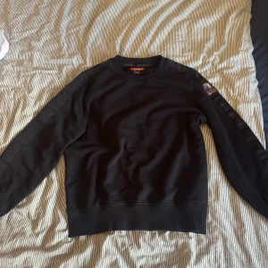 Svart fleece-tröja från Parajumpers - Svart fleece-tröja från Parajumpers med rund hals och ribbade muddar. Snygg patch på ena ärmen och diskreta detaljer längs ärmarna. Perfekt för dig som gillar stilrena och bekväma plagg med en sportig touch.