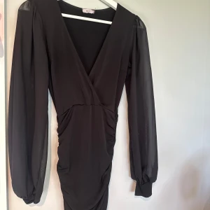 Svart omlottklänning från Nelly - Supersnygg svart kortklänning från Nelly med omlott och v-ringning. Klänningen har långa puff ärmar och ger en fin look. Har endast använt den en gång. Storlek xss men passar både xs/s eftersom de är stretchigt material🌺