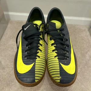 Nike CR7 inomhus fotbollsskor svart/gul - Säljer ett par Nike CR7 inomhus fotbollsskor i svart och gul med klassisk swoosh-logga och CR7-tryck på sidan. Skorna har snörning, platt sula och är designade för futsal eller inomhusspel. Snyggt mönster med gula linjer och detaljer.
