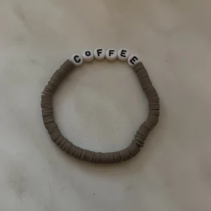 Brunt armband med texten COFFEE - Armband med bruna platta pärlor och vita bokstavspärlor som bildar ordet COFFEE. Perfekt accessoar för kaffeälskare som vill ha något personligt och stilrent på handleden.