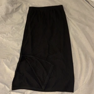 Svart ribbad kjol från Pieces - Svart långkjol från Pieces i ribbat material. Kjolen har en slits på ena sidan och är i storlek xs. 