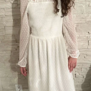 Vit långärmad klänning med prickigt mönster - Säljer en söt vit klänning med långärmade transparenta ärmar och små prickar. Klänningen har smock upptill och ett lätt, flowy tyg som ger en romantisk känsla. Perfekt för vår och sommar! Pris kan diskuteras.