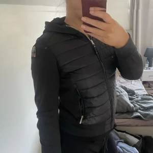 Svart jacka från Parajumpers - Säljer en svart jacka från Parajumpers med quiltad design och dragkedja. Jackan har en huva och är tillverkad i fleece och syntetmaterial. Perfekt för kyligare dagar. Använt sparsamt därav bra skick. Köpt på kids brand store för 3549kr. Storlek 176cm vilket motvarar ca M