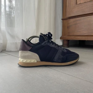 Valentino rockrunner - Säljer ett par Valentino Rockrunner sneakers i marinblå mesh och mocka med beige samt vinröda detaljer. (OPS finns en liten slitning på högra skon nere vid nitarna, se bild 4) men syns knappt. Hör av er vid minsta funderingar! Självfallet äkta!!!