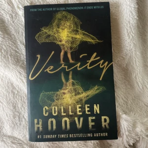 Verity - En psykologisk thrillerbok på engelska av Colleen Hoover. Omslaget är svart med guldfärgade detaljer och titeln 'Verity' i handskriven stil. Boken är en pocketutgåva och har en mystisk illustration på framsidan. Perfekt för dig som gillar spänning och oväntade vändningar.