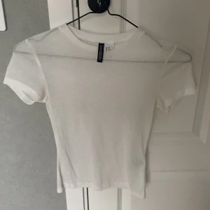 Vit t-shirt från H&M Divided - Oanvänd!!!!!En basic vit t-shirt från H&M Divided i en tight passform. T-shirten är kortärmad och tillverkad i mjuk bomull, perfekt att matcha med jeans eller kjol. Enkel och stilren design utan tryck eller mönster.