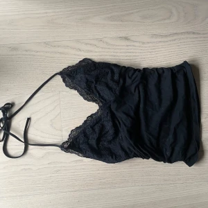 Svart spetslinne med tunna band - Säljer ett svart linne med tunna axelband och v-ringning. Köpt secondhand men aldrig använd av mig. Skulle uppskatta storleken runt M