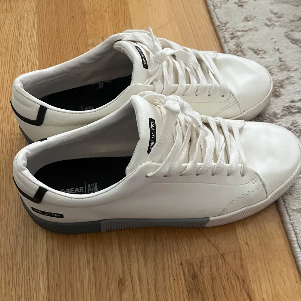 Säljer ett par stilrena vita sneakers från Pull&Bear med svarta detaljer och snörning. Skorna har rund tå och platt sula, perfekta för en clean och modern look. De är helt nya och används ett par gånger, de har kostat 450kr jag säljer de för 200 ( vid snabb köp kan priset diskuteras). Kengät.