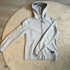Zip-Hoodie Björn Borg - Snygg ljusgrå hoodie från Björn Borg med dragkedja framtill och huva med snörning. Perfekt för en avslappnad stil. Ordinarie pris 1100kr