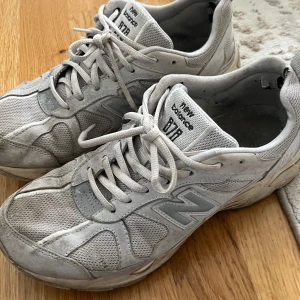 Grå New Balance  sneakers - Säljer ett par klassiska grå New Balance 877 sneakers med mesh och syntetpaneler. Skorna har snörning, rund tå och platt sula. Perfekta för en sportig och avslappnad stil.