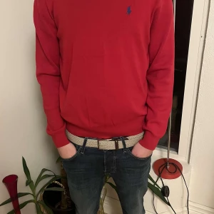 Röd tröja från Ralph Lauren - Säljer en klassisk röd tröja från Ralph Lauren med blå logga broderad på bröstet. Tröjan har rund halsringning och långa ärmar. Perfekt för dig som gillar stilrena och tidlösa plagg. Personen på bilden är 180cm och väger 67kg.