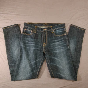 Mörkblå jeans från Nudie Jeans - Säljer ett par klassiska mörkblå jeans från Nudie Jeans med kontrastsömmar och ikonisk broderad bakficka. Jeansen har fem fickor, gylf och slimade ben. Perfekta för dig som gillar stilrena och tidlösa jeans.