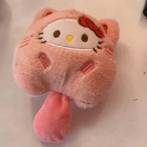 Rosa Hello Kitty nyckelring - En liten nyckelring i form av Hello Kittys ansikte, gjord i mjuk rosa plysch med broderade detaljer och öron. Nyckelringenhar en nyckelring i guldmetall och en liten svans. Perfekt som accessoar till väskan eller nycklarna.