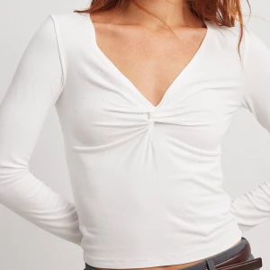 Vit långärmad topp med twistad detalj - Säljer en vit långärmad topp med snygg twistad detalj framtill och djup v-ringning. Enkel och stilren design som funkar till många tillfällen. Ligger i perfekt condition helt oanvänd 