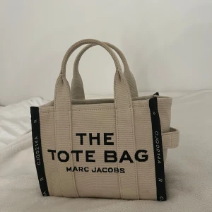 Beige tote bag från Marc Jacobs - en jätte snygg väska från Marc Jacobs💞 Väskan är köpt på ”Miinto” och är i mycket bra skick, endast använd fåtal gånger😇 extra band och tygpåsen den skickades i medföljer, samt prislappen och en extra lapp med extra information. kan skicka kvitto på att den är köpt på miinto och den är alltså helt äkta. Allting som originalt medföljer, skickas med väskan. den är lite smutsig på botten, kan skicka bild på det. Nypris ca 4000 på zalando och miinto, väskan är i en något mindre modell.