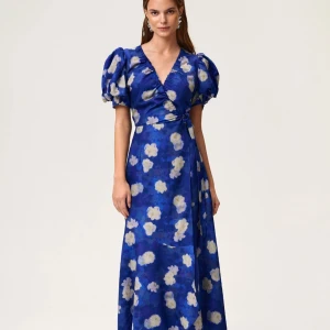 Adoore klänning Strl 34 - Säljer en blå långklänning med vita och ljusgula blommor. Klänningen har v-ringning, puffiga kortärmar och omlottliv med knyt i sidan. Perfekt för sommarens tillfällen när du vill sticka ut lite extra.