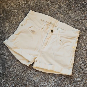 Beige bomullsshorts med uppvikta ben - Snygga beige shorts i bomull med klassisk femficksdesign och uppvikta ben som har bara lågt i garderoben. Perfekta för varma dagar och har en enkel knappstängning framtill. Passar till det mesta och är lätta att matcha.