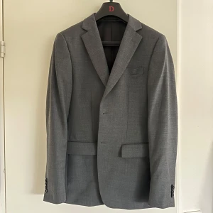 Mörkgrå kostym från Dressmann - Säljer en mörkgrå wool stretch kostym, slim fit från Dressmann då den blivit för liten. Passar perfekt till bal eller student. Storlek 46R på kavajen och 33/34 på byxorna. 