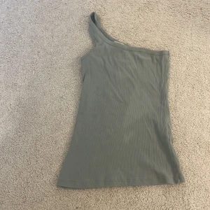 Grön ribbad oneshoulder topp från Modström - Säljer en stilren grön ribbad oneshoulder topp från Modström i storlek XS. På grund av att jag inte använder den längre. Den är i mycket fint skick och är använd ett fåtal gånger.