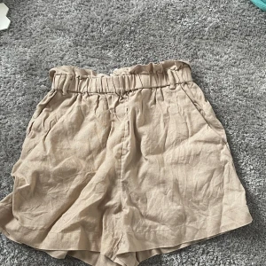Beiga linneshorts från & Other Stories - Snygga beiga shorts i linne från & Other Stories med hög midja i beige. Shortsen har fickor både fram och detalj fickor bak och en avslappnad passform. Perfekta för varma dagar!