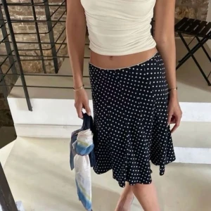 Svart prickig kjol - Säljer en svart kjol med vita prickar och lätt utsvängd form. Kjolen har en mjuk och följsam passform som ger en snygg siluett. Perfekt att styla med en enkel topp för en trendig look.