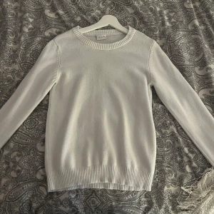 Vit stickad tröja från Vila - Säljer en klassisk vit stickad tröja från Vila med rund halsringning och ribbade muddar vid ärmslut och nederkant. Perfekt basplagg som passar till många olika outfits.