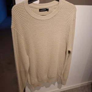 Beige stickad tröja från J.Lindeberg - Säljer en beige stickad tröja från J.Lindeberg. Tröjan har en rund halsringning och ett grovt ribbat mönster. Perfekt för kyligare dagar och enkel att matcha med olika outfits. Nypris 1500 kr