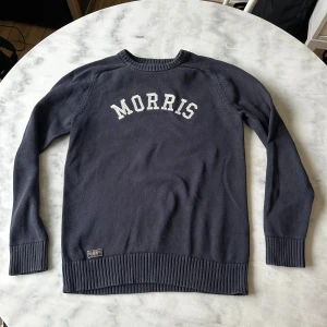 Mörkblå stickad tröja från Morris Gents - Säljer en mörkblå stickad tröja från Morris Gents med vit text på bröstet. Tröjan har rund halsringning, långa ärmar och ribbade muddar vid ärmslut och nederkant. Perfekt för en stilren och avslappnad look. Fint använd skick. 