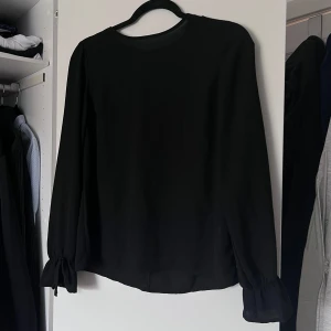 Svart blus från Gina Tricot - Säljer en svart tunn blus från Gina Tricot. Blusen har snören vid handlederna som går att dra ihop och knyta till fina små rosetter. Knäppning bak och lätt tyg. Perfekt för en middag eller annan festlighet. Knappt använd! ❤️ Önskar du veta exakta mått? Tveka inte att höra av dig!
