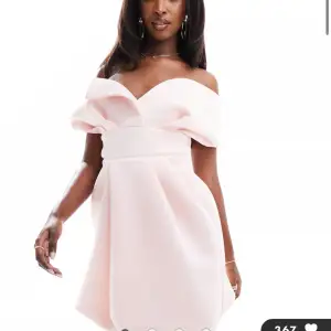 Superfin ljusrosa klänning med offshoulder och stora volangdetaljer upptill. Klänningen har en markerad midja och en kort, något utsvängd kjol. Perfekt för speciella tillfällen när du vill sticka ut. 