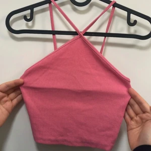Rosa ribbad croppad linnetopp - Säljer en rosa croppad linnetopp med smala axelband som korsas i ryggen. Toppen är ribbad och har en enkel, stilren design som passar perfekt till sommaren.