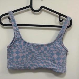 Blå och rosa mönstrad linnetopp från Pull&Bear - Säljer en ribbad linnetopp från Pull&Bear i blått och rosa med ett coolt, psykedeliskt rutmönster. Toppen har breda axelband och är perfekt för sommaren. Superfin att styla till både jeans och kjol!