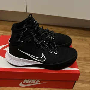 Nike Kyrie Irving Flytrap 4 Skor - Snygga svarta Nike sneakers med vit sula och svarta snören med vita detaljer. Skorna har en tydlig Nike-logga på sidan och är perfekta för basket eller träning. Sulan har svarta prickar för extra stil. 