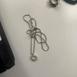 Silvrigt halsband från SNÖ - Säljer ett stilrent silverfärgat halsband med en unik solformad berlock dekorerad med små stenar. Kedjan är tunn och smidig, perfekt för att ge en extra touch till din outfit. Skriv privat för fler frågor osv💗💗