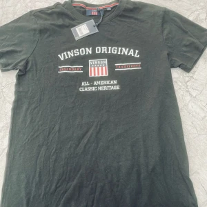 Svart t-shirt från Vinson Original - Svart t-shirt från Vinson Original med vit och röd text och tryck framtill. Klassisk rund halsringning och korta ärmar. Perfekt för en avslappnad stil.