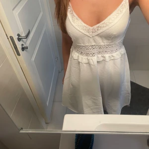 Vit spetsklänning med v-ringning - Säljer en söt vit klänning med v-ringad hals och fina spetsdetaljer vid byst och midja. Klänningen är ärmlös med smala axelband och har en luftig, kort kjol. Perfekt för sommarens alla tillfällen!