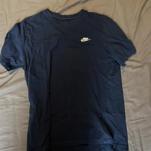 Mörkblå t-shirt från Nike - Säljer en mörkblå t-shirt från Nike med klassisk vit logga på bröstet. T-shirten har rund halsringning och är tillverkad i mjukt bomullsmaterial. Perfekt för en sportig och avslappnad stil.