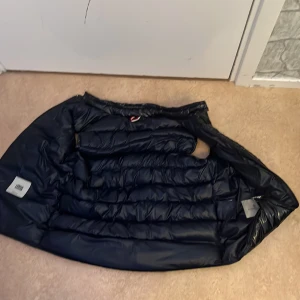 Mörkblå dunväst från Moncler - Säljer en mörkblå dunväst från Moncler med klassisk  dragkedja framtill. Perfekt för kyliga dagar och riktigt snygg till streetwear-stilen.