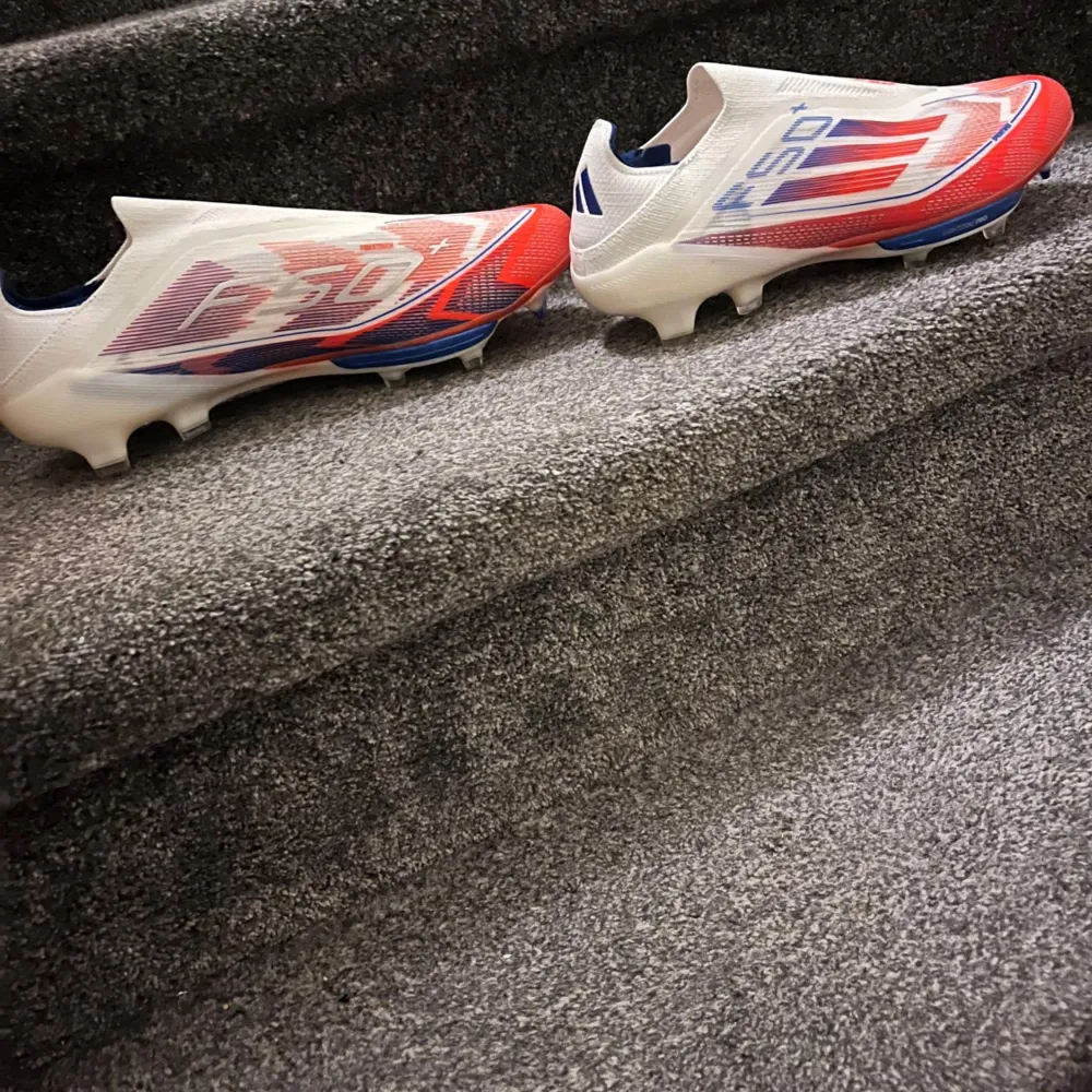 Snygga Adidas F50 fotbollsskor i vitt, rött och blått. Perfekta för snabba spelare som vill ha lättviktiga skor med bra passform.. Kengät.