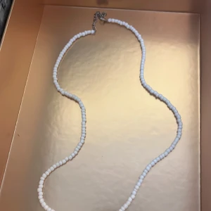 Vitt pärlhalsband - Säljer ett stilrent halsband med små vita pärlor och silverfärgat spänne. Perfekt för att ge en enkel men elegant touch till din outfit.