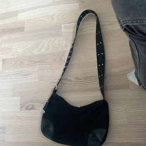 Svart axelväska från Weekday - Säljer en svart axelväska från Weekday med axelrem dekorerad med silvriga nitar. Jag säljer den eftersom att jag redan har många väskor. Priset kan diskuteras.