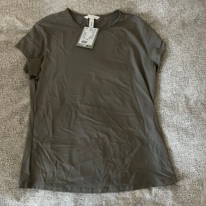 Olivgrön t-shirt från H&M - Säljer en olivgrön t-shirt från H&M i storlek M. T-shirten har rund halsringning och korta ärmar. Materialet känns mjukt och lätt mot huden. Tyvärr aldrig använd och prislapp finns kvar 