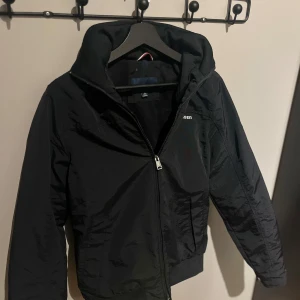Tommy Hilfiger  - Snygg svart stilren jacka. Luva går att veckla ut från nacken. Den e vind och vatten tät och nästan aldrig använd! Kom privat för mer info.