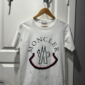 Moncler T-shirt - Vit moncler T-shirt med logga på framsidan och armen. Den är lite använd men är i bra skick. Skriv gärna för bilder eller om ni har andra frågor!