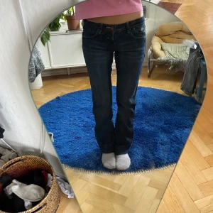 Lowwaist mörkblå bootcut jeans - Säljer ett par lowwaist mörkblå bootcut jeans med as snyggt broderi på bakfickorna och unik röd knapp vid gylfen.  Tycker själv att jeansen är supersnygga men har redan ett par liknande så därav säljer jag de!.