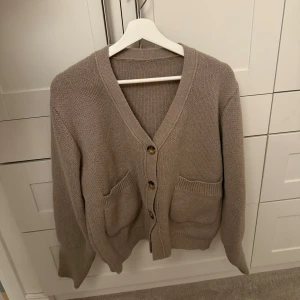 Beige stickad kofta med knappar - Mysig beige stickad kofta med v-ringning och stora fickor framtill. Koftan har långa ärmar och stängs med tre knappar. Aldrig använd🩷