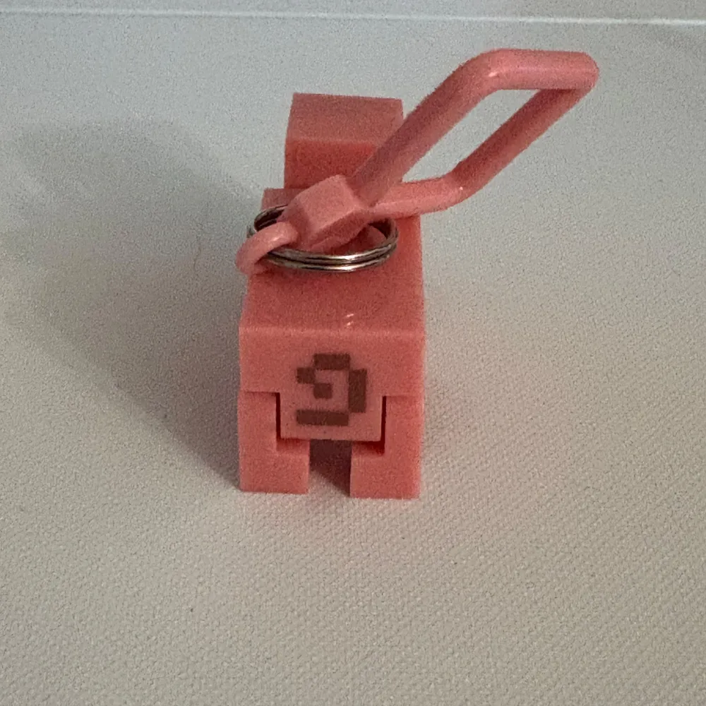 Säljer en söt nyckelring i form av en gris från Minecraft. Nyckelringen är rosa och har en fyrkantig, pixlig design som påminner om spelet. Perfekt att hänga på väskan eller nycklarna för alla Minecraft-fans!. Asusteet.